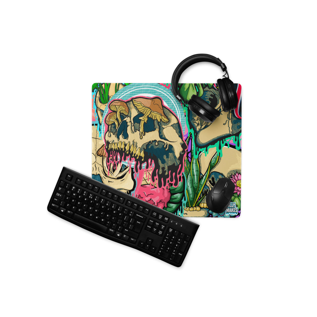 Product mockup of Illymakes gaming mousepad with a colorful collage of dripping skulls, mushrooms, and florals, shown with a keyboard, mouse, and headphones.