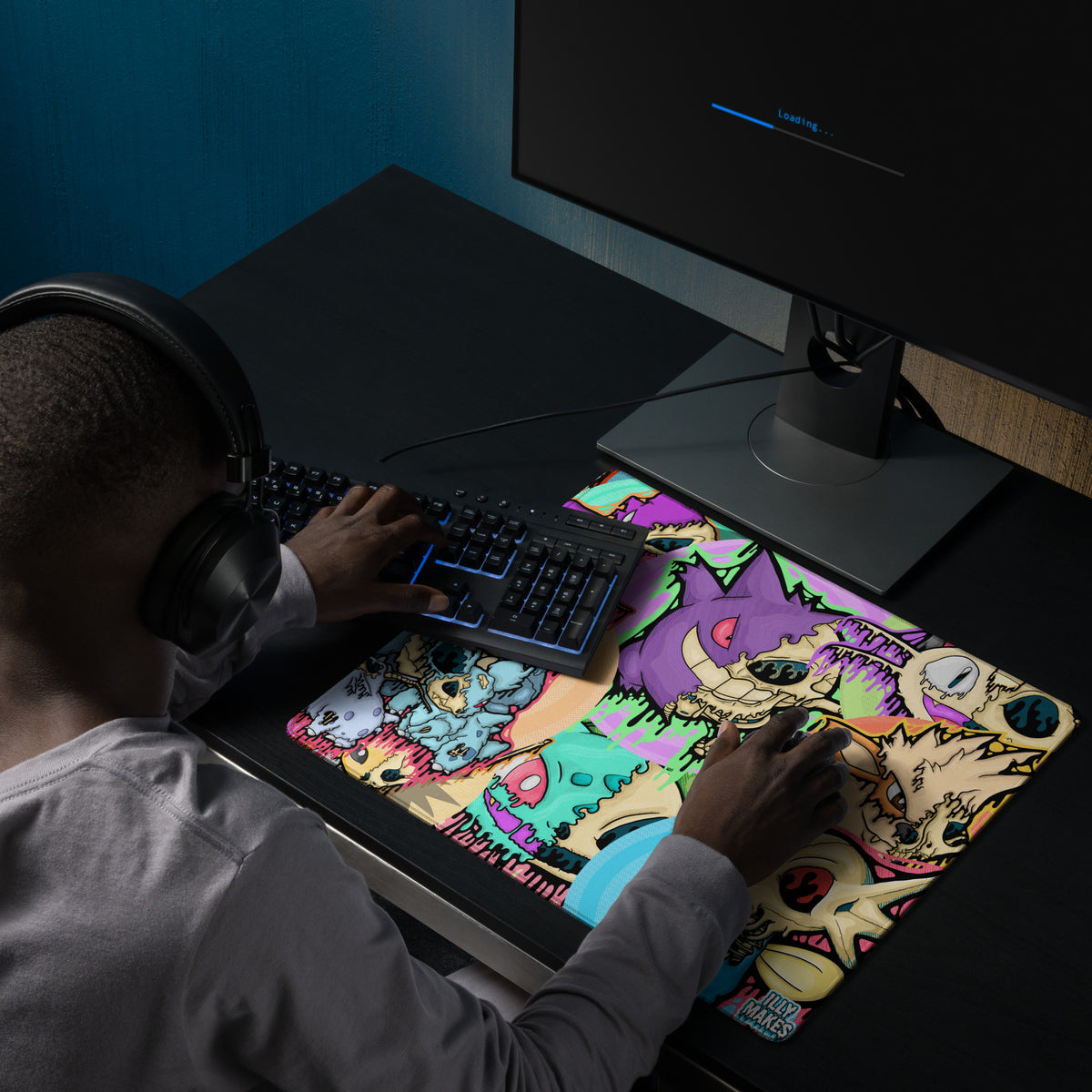Gamer using an 18 × 16-inch Drippy Pokémon Skull Collage mousepad beside a keyboard on a dark desk.