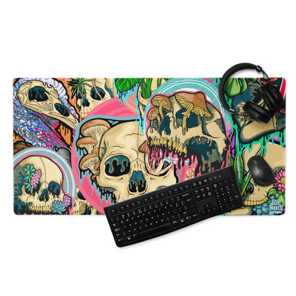 Product mockup of Illymakes gaming mousepad with a colorful collage of dripping skulls, mushrooms, and florals, shown with a keyboard, mouse, and headphones.