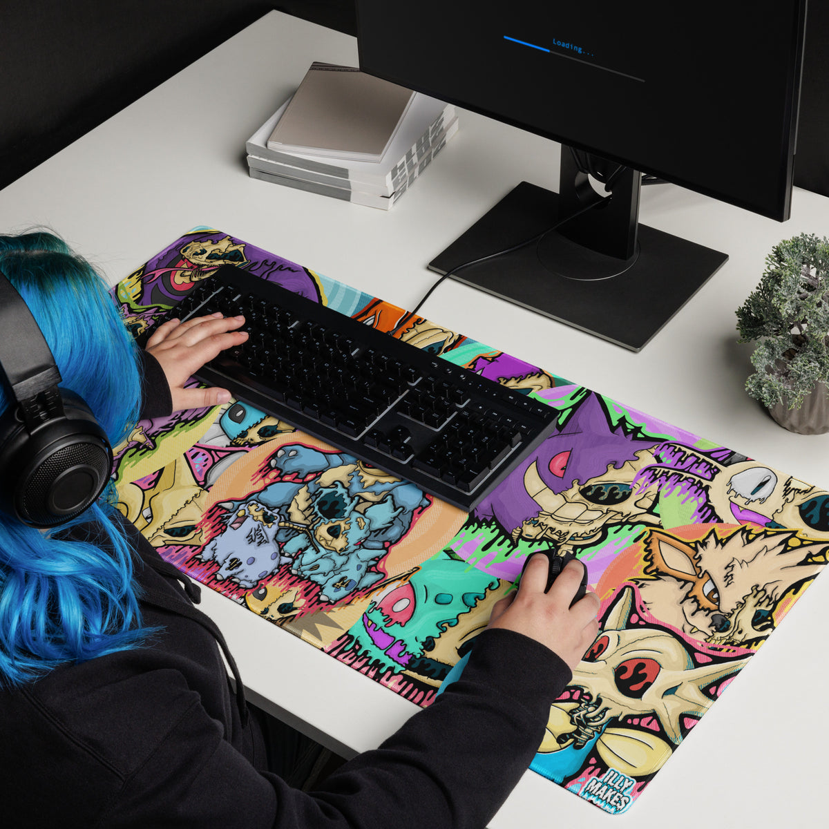 Gamer with blue hair using a large Drippy Pokémon Skull Collage mousepad beneath a black keyboard and mouse on a white desk.